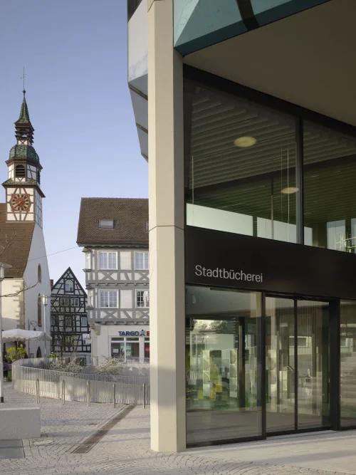 Moderne Stadtbibliothek mit Glasfassade, daneben historischer Turm und Fachwerkhäuser. (KI generiert)
