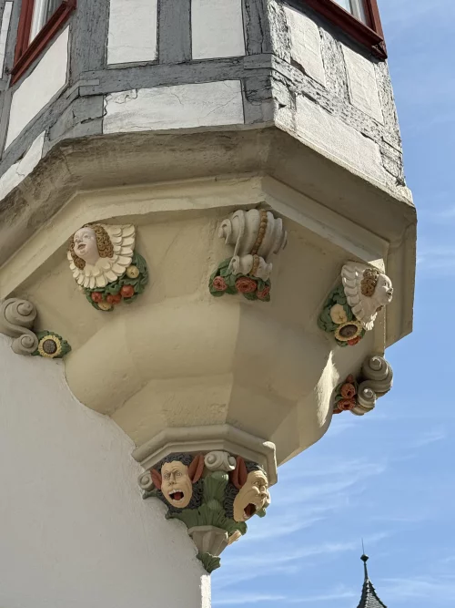 Ein Gebäude mit verzierten Gesichtern und Blumen an der Ecke. (KI generiert)