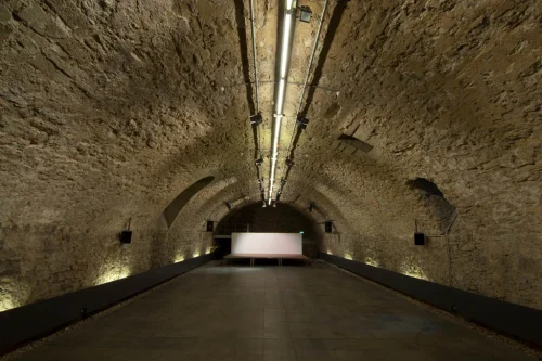 Ein langer, beleuchteter Tunnel mit Steinwänden und einem hellen Bildschirm am Ende. (KI generiert)