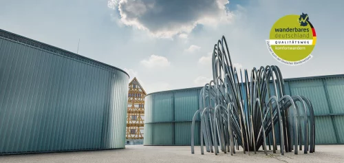 Moderne Metallskulptur vor Industriegebäuden, Wanderzeichen im Himmel. (KI generiert)