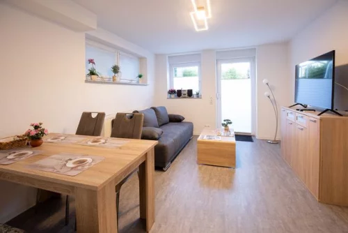 Wohnzimmer mit Esstisch, Stühlen, Sofa, TV und Pflanzen. Hell und modern eingerichtet. (KI generiert)