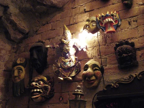 Verschiedene Masken und Figuren an einer Steinwand befestigt, beleuchtet. (KI generiert)