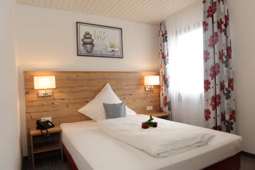 Ein gemütliches Hotelzimmer mit einem Doppelbett und Blumen auf der Bettdecke. (KI generiert)