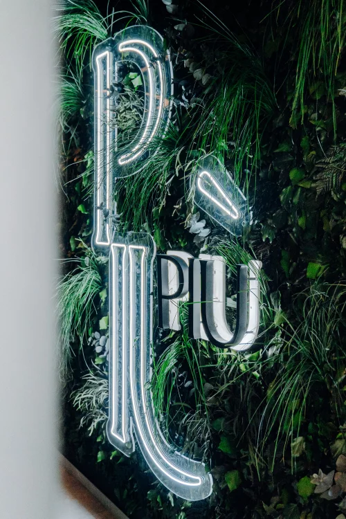 Leuchtende Buchstaben "PLAY" in einer grünen Pflanzenwand integriert. (KI generiert)