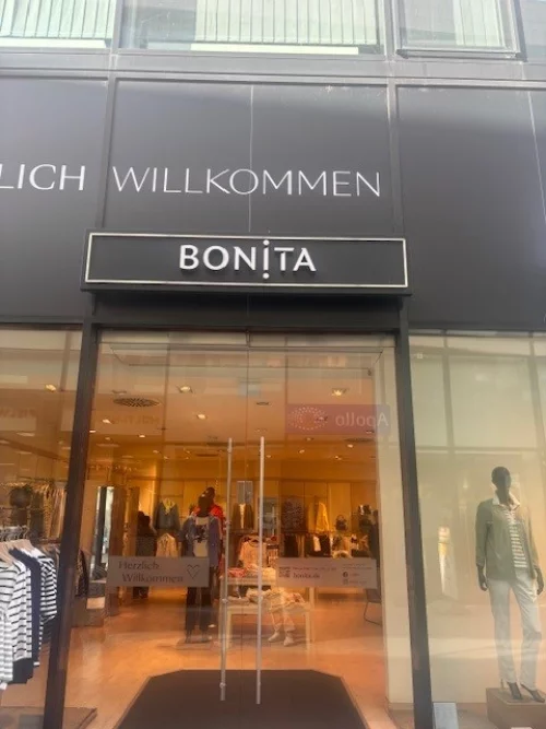 Eingangsbereich eines Ladens mit Schaufenster, Schriftzug 'BONITA' und 'HERZLICH WILLKOMMEN'. (KI generiert)
