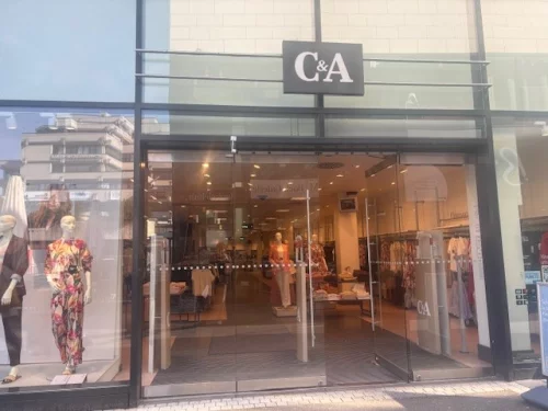 C&A-Eingang mit Schaufensterpuppen in Herbstmode, leere Einkaufsstraße. (KI generiert)