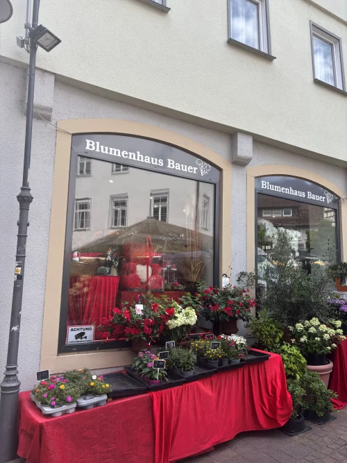 Blumenladen Blumenhaus Bauer mit roten Blumenarrangements vor dem Eingang. (KI generiert)