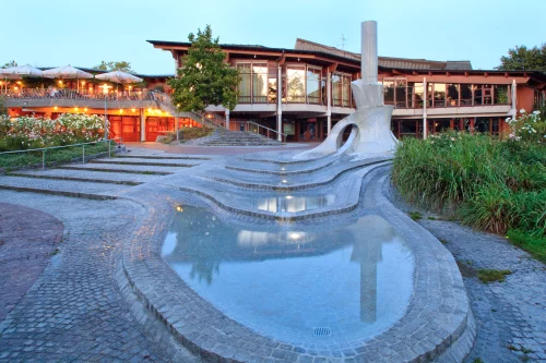 Moderne Architektur mit Brunnen und Stufen, umgeben von Pflanzen und beleuchteten Terrassen. (KI generiert)